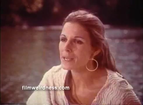 The still features a woman with long hair, wearing a light-colored sweater. She appears to be engaged in conversation, with a slightly intense expression. The background suggests a natural setting, possibly near water, adding to a serene yet reflective mood. The overall tone hints at emotional depth typical of dramatic scenes in films.