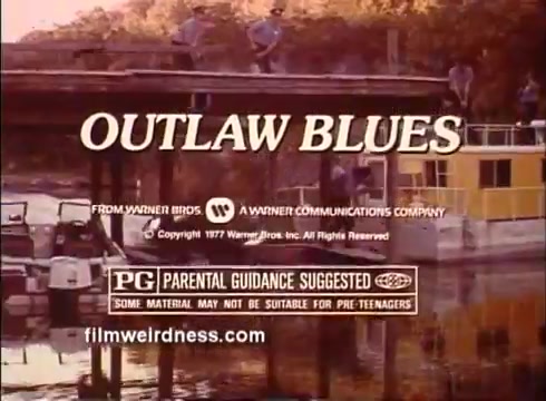 The still features the title 'OUTLAW BLUES' prominently displayed at the top, indicating the film's title. Below it, there are production credits mentioning Warner Bros. and a copyright notice from 1977. The film is rated PG, suggesting parental guidance is recommended. The backdrop appears to be a scene by the water with a dock, hinting at a setting relevant to the film's plot. The overall tone is nostalgic, representative of the 1970s era in which the film was released.