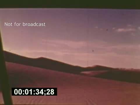 The 16mm still from 'Sixty Second Spot' captures a serene desert landscape, showcasing rolling sand dunes under a pastel sky. The image features a timestamp and a watermark stating 'Not for broadcast,' indicating its use in production rather than for public airing. This scene likely represents the setting for a 7-Up commercial, illustrating the film’s focus on the process of creating a television ad from inception to filming, reflecting mid-1970s production styles.