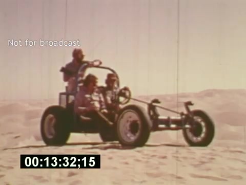 The still from the film 'Sixty Second Spot' captures a scene from the creation of a 7-Up commercial, showcasing a group of individuals in a dune buggy on a sandy landscape. The setting suggests an adventurous and playful tone, characteristic of mid-1970s advertising. The image conveys the behind-the-scenes process of filming, highlighting the casual and creative atmosphere of the time. The 'Not for broadcast' label emphasizes its archival nature, while the timecode indicates an ongoing scene in the production.