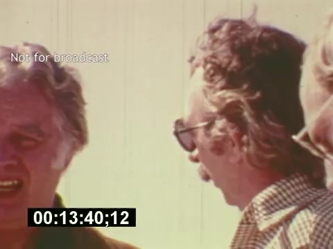 The still from 'Sixty Second Spot' captures a behind-the-scenes moment in the making of a 7-Up commercial from the mid-1970s. It features two men engaged in conversation, showcasing the candid, informal atmosphere of production. The film documents the entire process, from script development to casting and filming, culminating in the finalized advertisement. The timestamp suggests it's highlighting a specific scene in this creation journey. Overall, it offers a glimpse into the collaborative effort involved in crafting a TV commercial during this era.