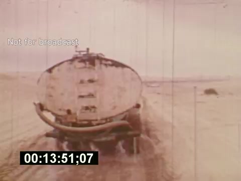 The 16mm still from 'Sixty Second Spot' features a vintage scene showing a large vehicle—likely a tank or trailer—moving along a dusty, deserted road. The pale color palette and date stamp suggest it captures a moment from the mid-1970s production of a 7-Up commercial. This segment highlights the behind-the-scenes process of creating a TV commercial, emphasizing the practical aspects of filming in an outdoor setting.