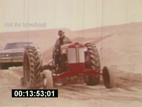 The still from 'Sixty Second Spot' depicts a scene where a man operates a tractor in a sandy landscape, with a car visible in the background. This film explores the process of creating a 7-Up commercial in the mid-1970s, highlighting elements like scripting, casting, and filming. The visual captures a blend of rural and commercial themes, reflecting the creative journey behind television advertising during that era.
