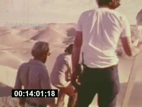 The still from 'Sixty Second Spot' captures a behind-the-scenes moment in the creation of a 7-Up commercial from the mid-1970s. It shows a group of filmmakers on a sandy desert set, possibly during a location shoot. One person is prominently leading the way, while others assist and observe. The image highlights the collaborative effort involved in commercial production, reflecting the era's filmmaking style. The 'Not for broadcast' label suggests it’s intended for internal use or archival purposes, emphasizing the film's documentary nature.