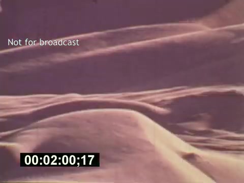 The still from 'Sixty Second Spot' showcases a visually striking desert landscape, characterized by soft, undulating sand dunes. The color palette leans towards warm, muted tones, evoking a nostalgic feel typical of mid-1970s filmmaking. The timestamp indicates the scene's timing within the film, suggesting it may serve as a transition or backdrop related to the commercial's thematic elements. Notably, the text 'Not for broadcast' reflects its exclusive and behind-the-scenes nature, highlighting the creative process behind the making of a 7-Up commercial.