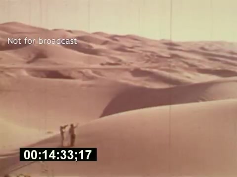 The 16mm still from 'Sixty Second Spot' depicts a desert landscape with two figures in the distance. The scene captures a moment in the creation of a 7-Up commercial, highlighting the setting and atmosphere intended for the advertisement. The film explores the process of commercial production from the initial script to casting and filming, emphasizing the artistic and logistical elements involved. The text 'Not for broadcast' suggests this is a behind-the-scenes look intended for archival purposes rather than public viewing.