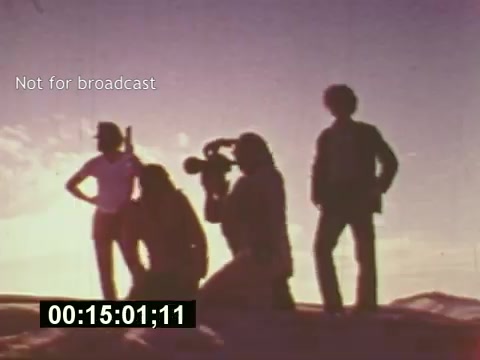 The still from 'Sixty Second Spot' captures a moment in the filmmaking process for a 7-Up commercial from the mid-1970s. It features silhouettes of crew members against a vibrant sunset, with one person operating a camera. The scene conveys the creative energy and teamwork involved in commercial production, showcasing the behind-the-scenes effort that brings a script to life. The timestamp suggests this is a pivotal moment in the documentary, emphasizing the art of filmmaking.