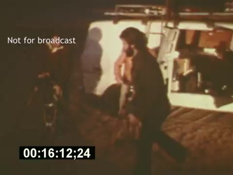 The still from 'Sixty Second Spot' captures a moment behind the scenes of a 7-Up commercial production from the mid-1970s. The image shows crew members engaged in the filmmaking process, with one individual prominently walking while others are in the background, likely handling equipment. The setting appears to be outdoor, characterized by a casual atmosphere typical of film shoots of that era. The 'Not for broadcast' label suggests this is a behind-the-scenes clip, focusing on the creative process from script to filming.