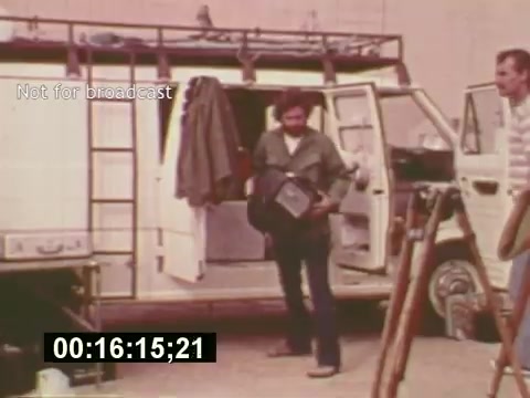 The still from 'Sixty Second Spot' depicts a moment during the creation of a 7-Up commercial in the mid-1970s. It features a crew member exiting a van, suggesting on-location filming. The scene highlights the behind-the-scenes process, showcasing the casual, somewhat rugged environment typical of commercial shoots of that era. The timestamp at the bottom indicates a specific moment within the film, emphasizing its documentary style.