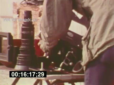 The still from 'Sixty Second Spot' captures a behind-the-scenes moment in the creation of a 7-Up commercial. It shows a crew member working with film equipment, emphasizing the intricacies of production in the mid-1970s. The shot highlights the technical aspects of filmmaking, including camera gear and setup, while conveying a sense of authenticity and craftsmanship in advertising. The timestamp, '00:16:17;29,' suggests this is part of the documentary's exploration of the commercial's development process.