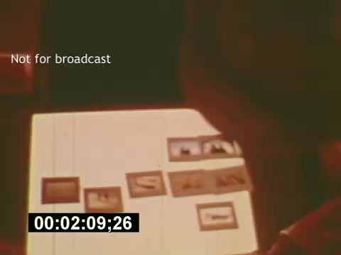 The still from 'Sixty Second Spot' captures a moment in the filmmaking process of a 7-Up commercial from the mid-1970s. It depicts a person reviewing a series of small images or storyboards laid out on a table, likely involved in planning or organizing shots for the commercial. The setting conveys a behind-the-scenes look at the creative process, as it explores the journey from script development to casting and filming. The timestamp at the bottom suggests it is a specific scene in the film, and the text indicates the clip is not meant for broadcast.