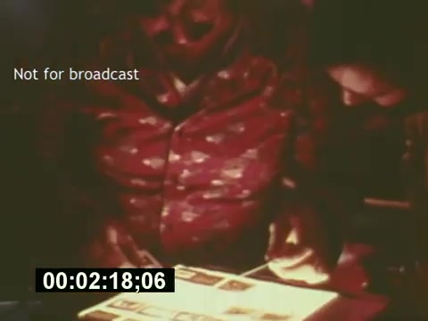 The still from 'Sixty Second Spot' captures a behind-the-scenes moment in the creation of a 7-Up commercial from the mid-1970s. It features two individuals examining film stills, likely during the pre-production phase. The warm lighting gives a nostalgic feel, emphasizing the creative process involved in commercial filmmaking of that era. The overlay text 'Not for broadcast' suggests this is an exclusive behind-the-scenes glimpse, not intended for public viewing. The timestamp indicates the specific moment in the film, enhancing its documentary aspect.