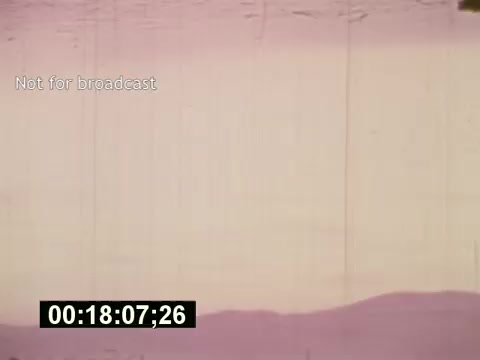 The still is from 'Sixty Second Spot,' a mid-1970s film documenting the creation of a 7-Up commercial. It showcases a moment in the production process, featuring a faded, pink-tinged landscape with clear tape marks, suggesting a raw, behind-the-scenes glimpse. The frame includes a timecode and a 'Not for broadcast' watermark, emphasizing its unedited, original state before final cuts. The film explores elements like scripting, casting, and filming techniques relevant to the era.