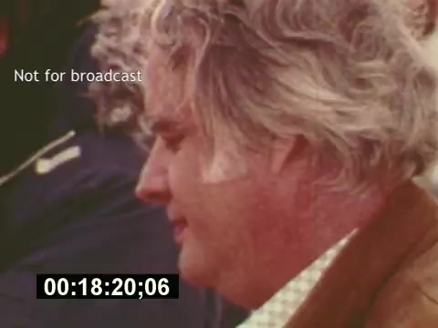 The still captures a moment from 'Sixty Second Spot,' a documentary that explores the making of a 7-Up commercial from the mid-1970s. It features a close-up of a man, likely involved in the production, as he appears focused and contemplative. The image includes a timestamp showing 18 minutes and 20 seconds into the film, and there's a label indicating it's 'Not for broadcast.' The context highlights the behind-the-scenes process of script development, casting, and filming, culminating in the final commercial presentation at the film's end.