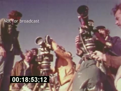 The still from 'Sixty Second Spot' captures a behind-the-scenes moment in the making of a 7-Up commercial from the mid-1970s. It features a group of filmmakers, equipment in hand, likely discussing shots or angles. The vibrant colors and retro aesthetic highlight the film's era, emphasizing the collaborative effort that goes into commercial production. A time code and 'Not for broadcast' label suggest its specific use in production rather than for public viewing.