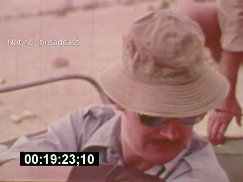 The still from 'Sixty Second Spot' shows a man wearing a bucket hat and sunglasses, possibly involved in the production of a 7-Up commercial. The scene captures a behind-the-scenes moment, reflecting the film's focus on the creative process of advertising in the mid-1970s, from scripting to casting and filming. The timestamp indicates it's part of the film's narrative, emphasizing the raw and informal elements of commercial production during that era.