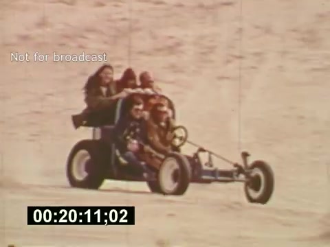 This 16mm still from 'Sixty Second Spot' captures a lively moment from the making of a 7-Up commercial. It features a group of people joyfully riding in a go-kart through a sandy terrain, highlighting the fun and adventurous spirit of the brand. The scene reflects the playful, carefree vibe typical of mid-1970s commercials, showcasing the creative process behind advertising. The timecode indicates it's part of a series of behind-the-scenes footage.