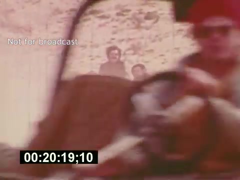 The still from 'Sixty Second Spot' captures a moment during the production of a 7-Up commercial in the mid-1970s. It features a close-up of a vehicle’s interior, possibly from the perspective of a driver, with two individuals partially visible in the background. The muted colors and vintage aesthetics reflect the era of the film, which documents the creative process, including script development, casting, and filming, ultimately leading to the release of the commercial. The timecode at the bottom indicates the specific moment in the film.