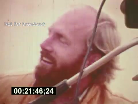 The still from 'Sixty Second Spot' captures a behind-the-scenes moment during the making of a 7-Up commercial from the mid-1970s. It features a bearded man, presumably a crew member or actor, wearing a warm smile and engaging in the creative process. The image highlights the informal and jovial atmosphere of filming, emphasizing collaboration in advertising production. The timestamp and 'Not for broadcast' label suggest it's a candid glimpse, not meant for public viewing, showcasing the raw energy of the filmmaking process.
