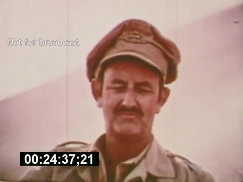 The still from 'Sixty Second Spot' captures a moment in the filmmaking process for a 7-Up commercial. It features a man wearing a military-style cap and a neutral expression, likely a cast or crew member involved in the production. The image is tinged with a vintage aesthetic typical of the mid-1970s, reflecting the era's film techniques. A timestamp and the note 'Not for broadcast' indicate it’s a behind-the-scenes capture rather than a finalized scene. The film provides insight into the commercial’s creation, demonstrating the journey from script to screen.
