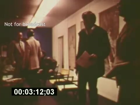 The still from 'Sixty Second Spot' captures a behind-the-scenes moment in the production of a 7-Up commercial from the mid-1970s. It features a group of people engaged in discussion, likely during a casting session or meeting. The setting appears to be an office or studio space, with chairs and posters adorning the walls. The atmosphere conveys the collaborative effort and planning involved in creating a television commercial, emphasizing the creative process behind advertising. The timestamp and 'Not for broadcast' note suggest it's an informal documentation of the production stages.