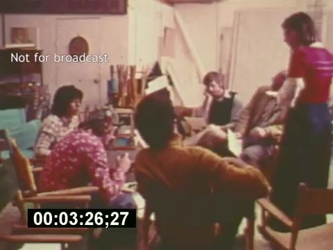 The still from 'Sixty Second Spot' captures a behind-the-scenes moment in the creation of a 7-Up commercial from the mid-1970s. The scene shows a diverse group of individuals seated in a casual setting, presumably brainstorming or discussing the commercial's concept. There’s a balance of engagement, with some people actively participating in the conversation while others listen. The atmosphere feels collaborative and creative. The timestamp indicates it's part of a documentary style, focusing on various stages, including script development, casting, and filmmaking. The 'Not for broadcast' label suggests it's intended for internal use or preview rather than public airing.