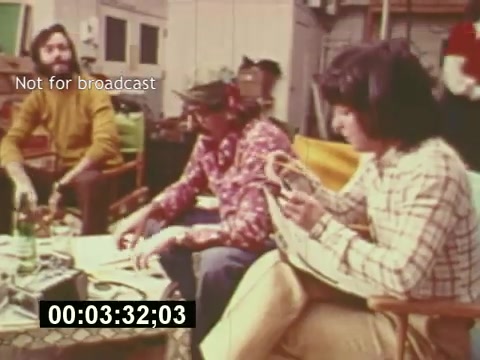 The still from **'Sixty Second Spot'** features a candid moment during the production of a 7-Up commercial. It shows three individuals engaged in the creative process, likely discussing concepts and ideas. The setting appears to be a relaxed workspace, with casual attire reflecting the mid-1970s vibe. This snapshot captures the collaborative spirit and behind-the-scenes dynamics of filmmaking during that era. The time code suggests it is part of a specific segment of the film, emphasizing that it's not intended for broadcast.
