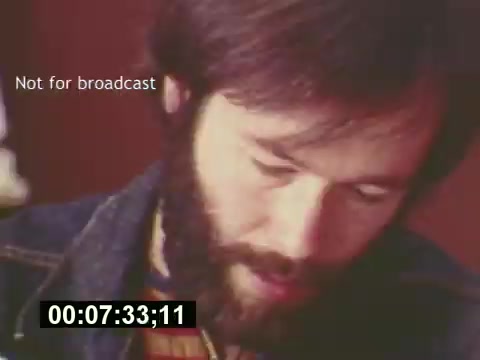 The still is from the film 'Sixty Second Spot,' depicting a scene in the creation of a 7-Up commercial from the mid-1970s. It shows a man with a beard, focused on a task, possibly reviewing a script or planning details related to the commercial. The timestamp indicates it's a moment of contemplation or creative process, emphasizing the behind-the-scenes efforts that go into making television advertisements during that era. The note 'Not for broadcast' suggests it's a behind-the-scenes shot not intended for public viewing.
