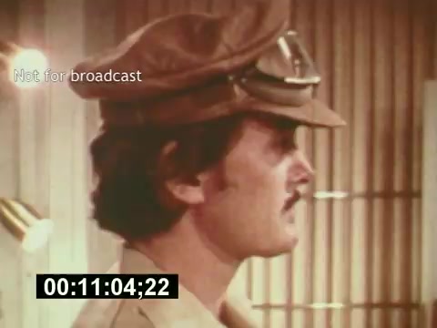 The still from 'Sixty Second Spot' features a male actor wearing a hat and glasses, characterized by a mustache. He appears to be in a creative or production setting, which aligns with the film's focus on the making of a 7-Up commercial. The overlay text 'Not for broadcast' indicates it's a behind-the-scenes take, capturing the actor's role in the process leading up to the final ad. The timecode suggests it’s an excerpt that provides insight into the filming aspects during the mid-1970s.