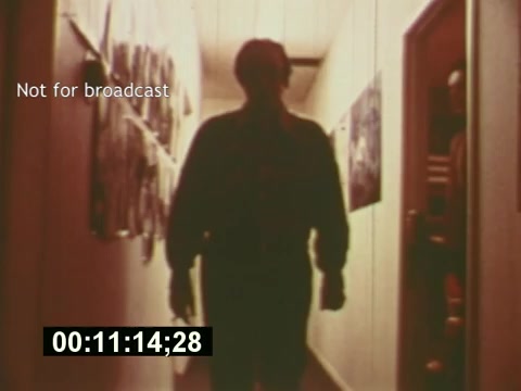 The still from 'Sixty Second Spot' depicts a silhouette of a figure walking through a corridor filled with posters or images on the walls. The lighting is warm and soft, creating a nostalgic feel that reflects the mid-1970s aesthetic. Overlay text indicates the footage is 'Not for broadcast,' and a timecode at the bottom suggests it's part of a longer segment. This moment likely captures the creative process leading to the production of a 7-Up commercial, emphasizing the behind-the-scenes aspects of television advertising during that era.