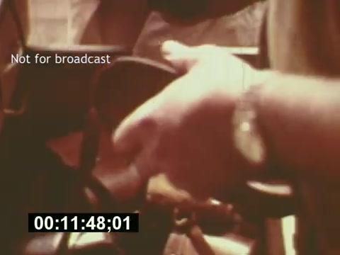 The still from 'Sixty Second Spot' captures a behind-the-scenes moment in the creation of a 7-Up commercial from the mid-1970s. It focuses on a person's hand holding equipment, suggesting the technical aspects of filming. The image reflects the process of production, showcasing the effort that goes into bringing a commercial to life, from script to casting and filming, and hints at the craftsmanship behind advertising in that era. The 'Not for broadcast' label emphasizes its use as an archival piece rather than for public viewing.