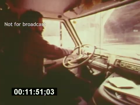 The still from 'Sixty Second Spot' features a man driving a vehicle, possibly a production van, with a focus on the dashboard and steering wheel. The vintage aesthetic captures the mid-1970s vibe, highlighting the behind-the-scenes process of creating a 7-Up commercial. A timecode overlay indicates the duration, and a 'Not for broadcast' label suggests it's a raw or unedited clip. The scene emphasizes the practical aspects of commercial production during that era.
