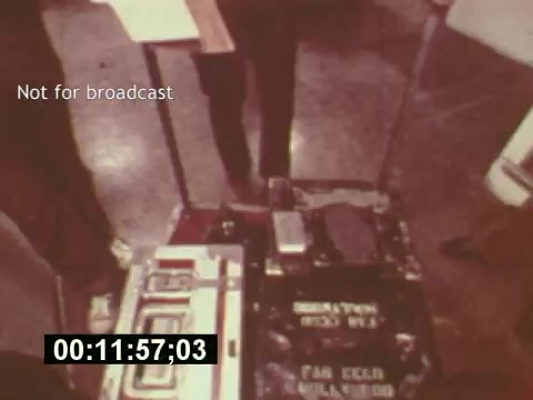 The still captures a moment during the production of a 7-Up commercial from the mid-1970s, showcasing equipment likely used for filming. It features a view of various cases and gear on a set, with a timer indicating the progress of the scene. The text 'Not for broadcast' implies this footage is behind-the-scenes material, emphasizing the creative process involved in bringing the commercial to life.