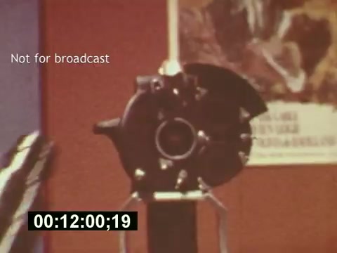 The still from 'Sixty Second Spot' features a close-up of a film camera, highlighting the technical aspects of creating a commercial. The setting suggests a behind-the-scenes look at the filmmaking process, with a focus on the preparation stages, including scripting, casting, and filming. The image includes a timestamp and a 'Not for broadcast' label, indicating that it's part of a documentary exploring the intricacies of producing a 7-Up advertisement. The vibrant colors and retro aesthetic reflect the mid-1970s era of television advertising.