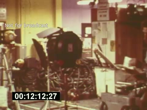 The still from 'Sixty Second Spot' portrays a behind-the-scenes glimpse of a film set dedicated to the creation of a 7-Up commercial from the mid-1970s. It shows film equipment, lighting setups, and an array of cables, highlighting the intricate technical preparations involved in commercial production. The time code at the bottom indicates a specific moment in the film, and the 'Not for broadcast' label suggests this is a restricted or private viewing. Overall, the image encapsulates the hustle of the filmmaking process, emphasizing the blend of creativity and technical skill necessary for commercial production.