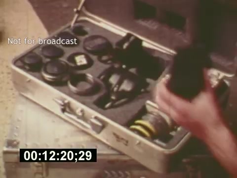 The still from 'Sixty Second Spot' features a camera case filled with lenses and filmmaking equipment, emphasizing the technical aspects of creating a 7-Up commercial. The scene captures the meticulous preparation involved in commercial production during the mid-1970s, showcasing the tools of the trade before the filming begins. The timestamp suggests this moment occurs mid-way through the film, highlighting the behind-the-scenes process of advertising creation.