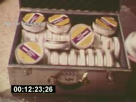 The still from 'Sixty Second Spot' shows a metallic case filled with circular film canisters, likely containing footage related to the production of a 7-Up commercial. Each canister is labeled, indicating they hold segments of the commercial, ranging from scripting to casting and filming. The scene captures a behind-the-scenes look at the filmmaking process from the mid-1970s, highlighting the meticulous organization required in commercial production. The timestamp and 'Not for broadcast' label suggest it is part of a documentary-style exploration rather than a final broadcast piece.