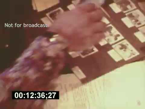 The still depicts a behind-the-scenes moment from the film 'Sixty Second Spot,' showcasing the creation of a 7-Up commercial from the mid-1970s. In the frame, a hand is seen above a spread of photographs and a script, emphasizing the casting and planning processes involved in the production. The text 'Not for broadcast' indicates the segment is intended for internal use. The timestamp hints at the film's progression, capturing the detailed and collaborative effort that goes into commercial filmmaking.