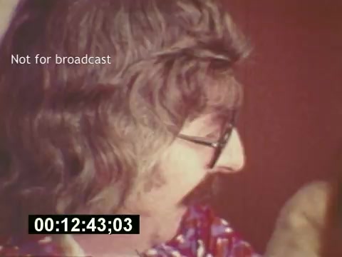 The still from 'Sixty Second Spot' captures a moment in the mid-1970s during the production of a 7-Up commercial. It features a man with distinctive long hair and glasses, possibly involved in the creative process, showcasing the lively and collaborative atmosphere of commercial filmmaking. The image includes a timestamp and a 'Not for broadcast' label, indicating it is intended for behind-the-scenes purposes. Overall, it reflects the era's unique style and the behind-the-scenes intricacies of advertising production.