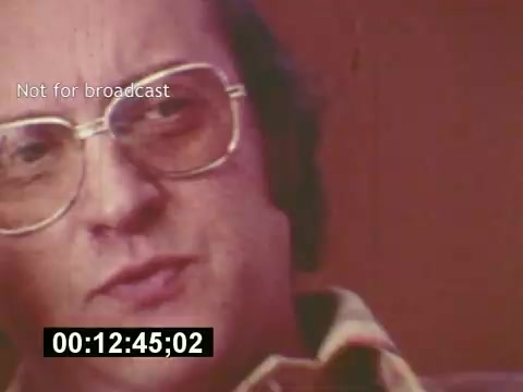 The still depicts a close-up of a man wearing large glasses, engaged in conversation. His expression suggests he’s sharing insights or experiences related to the filmmaking process. The background is softly focused, contributing to a retrospective or documentary feel. A timecode indicates the duration, and a watermark states 'Not for broadcast,' emphasizing the educational or behind-the-scenes nature of the footage. This captures a moment in the mid-1970s, reflecting the era's style and the subject matter of creating a 7-Up commercial.