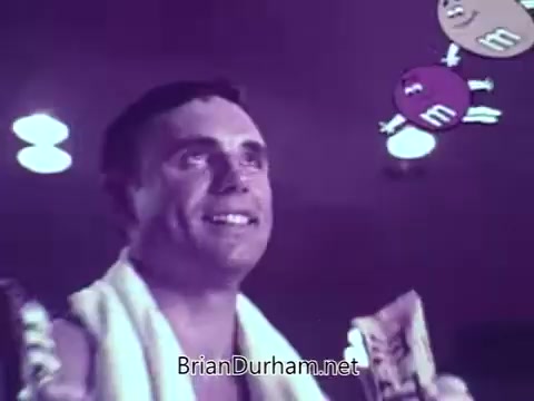 The still from the M&M's animated commercial features a smiling man with a towel around his neck, holding M&M's candy. Above him, animated M&M's characters float playfully, creating a fun and energetic atmosphere. The scene captures the lighthearted and humorous tone typical of the brand's ads, emphasizing enjoyment and excitement around the product.