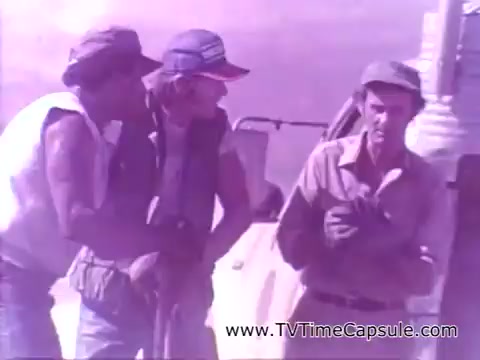 The still shows three men engaged in conversation, likely in a casual or working environment. They appear to be discussing something with interest, possibly related to their work. The setting reflects a rural or outdoor backdrop, contributing to the relaxed, everyday feel typical of Coca-Cola's advertising in that era. The overall tone suggests camaraderie and enjoyment, mirroring the slogan 'Have a Coke and a Smile.'