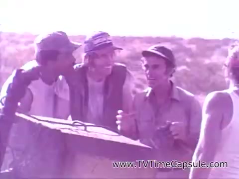 The still depicts a group of three men, likely in a rural or outdoor setting, engaging in a lively conversation. They appear cheerful and relaxed, suggesting camaraderie. The overall tone and colors evoke a nostalgic feel, aligning with the lighthearted theme of the 'Have a Coke and a Smile - Coke Adds Life' campaign, which emphasizes enjoying life and moments with friends.