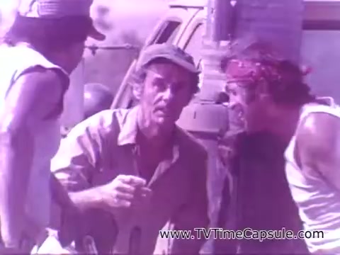 The still captures a scene from the Coca-Cola advertisement featuring three men engaged in conversation. They appear to be in a rural setting, gathered near a vehicle. The mood seems lighthearted and casual, emphasizing camaraderie. The iconic slogan 'Have a Coke and a Smile' suggests a theme of enjoyment and connection, typical of Coca-Cola’s marketing approach. The visual tone has a vintage feel consistent with its era.