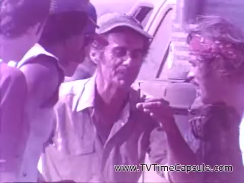 The still from the Coca-Cola commercial 'Have a Coke and a Smile - Coke Adds Life' features a group of individuals engaged in a lively interaction, likely conveying a sense of camaraderie and joy. The scene is informal, possibly set outdoors, with characters sharing smiles and a Coke, emphasizing the theme of refreshing enjoyment and connection that the brand promotes. The overall atmosphere is warm and inviting, showcasing how Coca-Cola can enhance moments of togetherness.