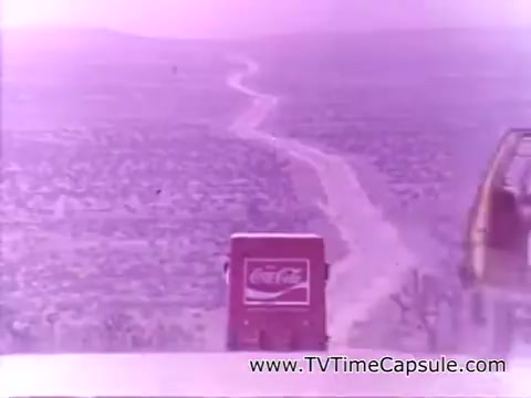 The still features a vintage Coca-Cola truck driving along a winding road that stretches through a vast, scenic landscape. The colors are predominantly pastel, giving it a nostalgic feel. This image is part of the 'Have a Coke and a Smile - Coke Adds Life' campaign, evoking themes of happiness, adventure, and the refreshing enjoyment of Coca-Cola.