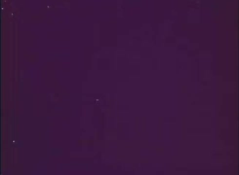 The still from 'Scandalous John' features a rich, purple background, indicative of a vintage 16mm print. The image lacks distinct characters or scenes, emphasizing a creative use of color and texture typical of promotional materials from that era. The overall composition suggests an atmosphere of intrigue or whimsy, aligning with the film's themes.