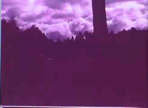 The still appears to feature a dramatic sky filled with billowing clouds, rendered in a striking purple hue. The foreground shows a silhouetted tree or structure, likely adding a sense of depth and framing to the scene. The overall mood suggests a stylized or atmospheric interpretation, characteristic of film promos.