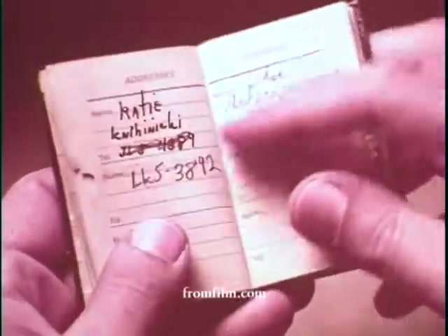 The still from the WCBS promo features a close-up of a hand flipping through a small address book. Notable details include handwritten entries, which show a name, 'Katie Kentinicki,' accompanied by a series of numbers, possibly a phone number or an identification code. The scene suggests an investigative or reporting context, highlighting the personal and detailed nature of crime reporting. The soft color tones typical of 1970s film are evident, enhancing the nostalgic feel of the image.