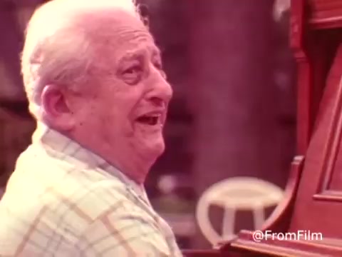 The still from the 1970s American Health Care Association commercial features an older man joyfully playing a piano, smiling widely. The warm tones and nostalgic aesthetics hint at a focus on community and enjoyment in care for the elderly. It captures a moment of happiness, emphasizing the positive aspects of healthy aging. .